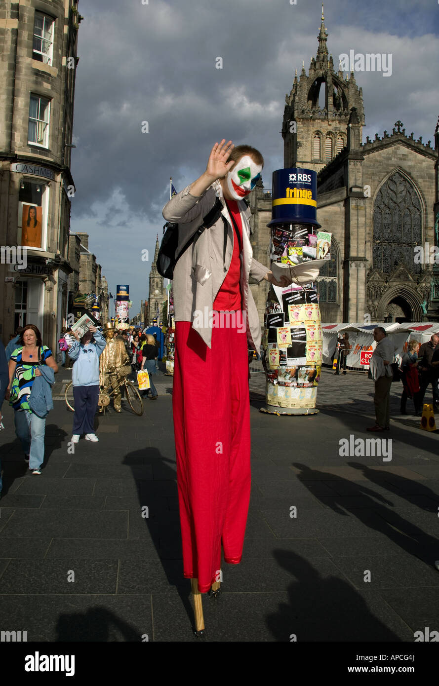 El Festival Fringe de Edimburgo, macho stilt walker olas manteniendo su sombrero con la Catedral de St Giles en segundo plano. Foto de stock