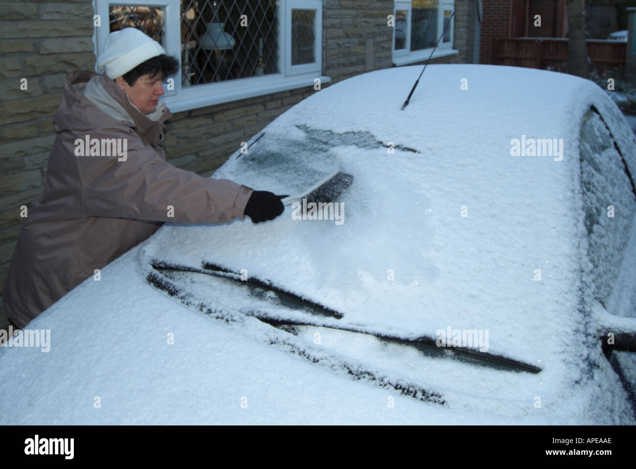 Mujeres en ropa de abrigo de invierno con cepillo para quitar la nieve antes de raspado de del parabrisas de Ford Ka estacionado en casa cochera de -