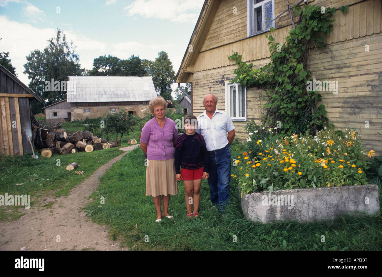 Una familia letona de pie enfrente de granja típica casa rural en Letonia Foto de stock