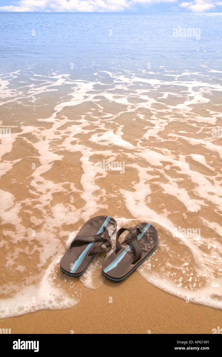 Un par de sandalias en una playa de arena dorada, siendo arrastrados al mar  ligero desenfoque de movimiento Fotografía de stock - Alamy