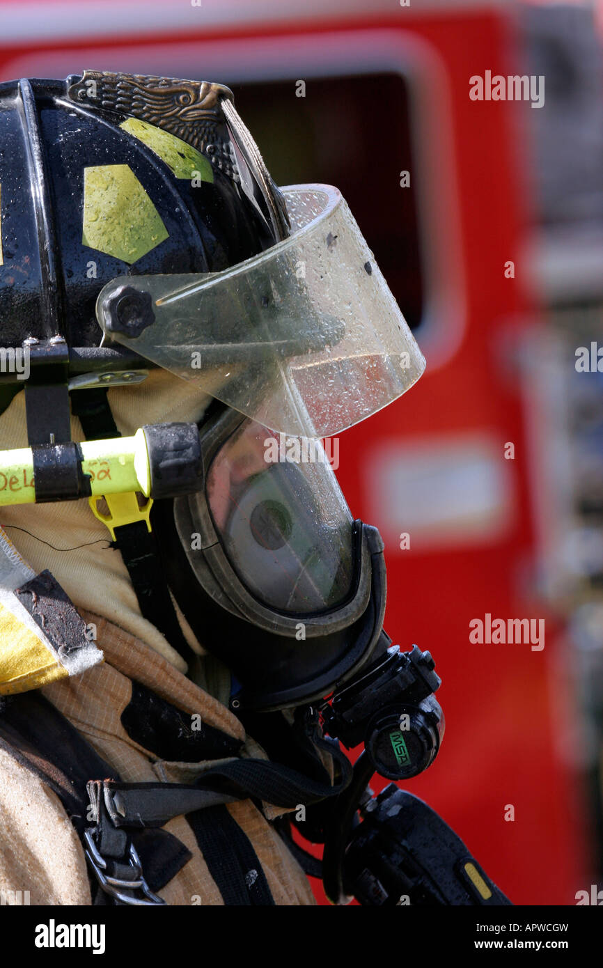 Un bombero posando delante del camión de bomberos todo mojado de agua pulverizada en la extinción del incendio de estructura Foto de stock