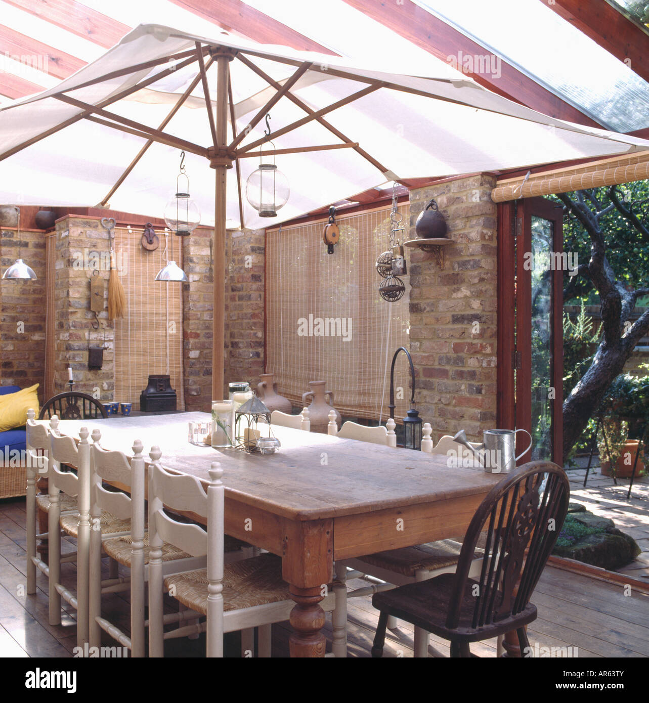 Jardín sombreado paraguas blanco mesa de madera de pino con rush sentados en sillas de comedor acristalado Foto de stock