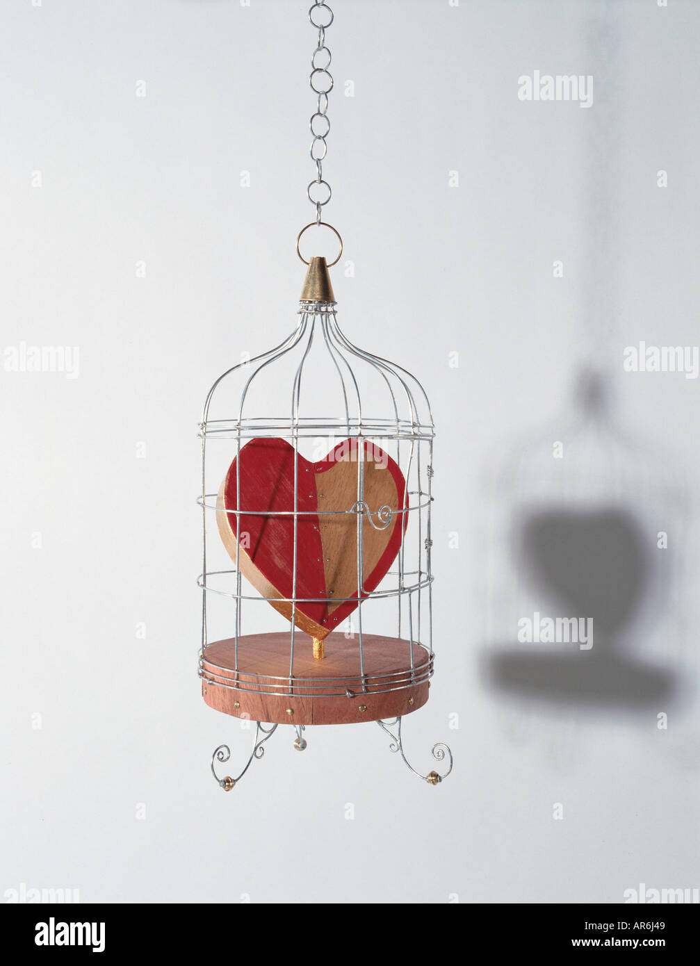 Amor de madera Colgante corazón atrapado en una forma de jaula de metal, corazón pintado mitad rojo, base de madera maciza Foto de stock