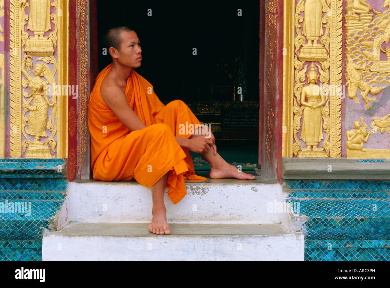 Monje sentado en el pórtico del templo, el Wat Xieng Thong, Luang Prabang, Laos Foto de stock