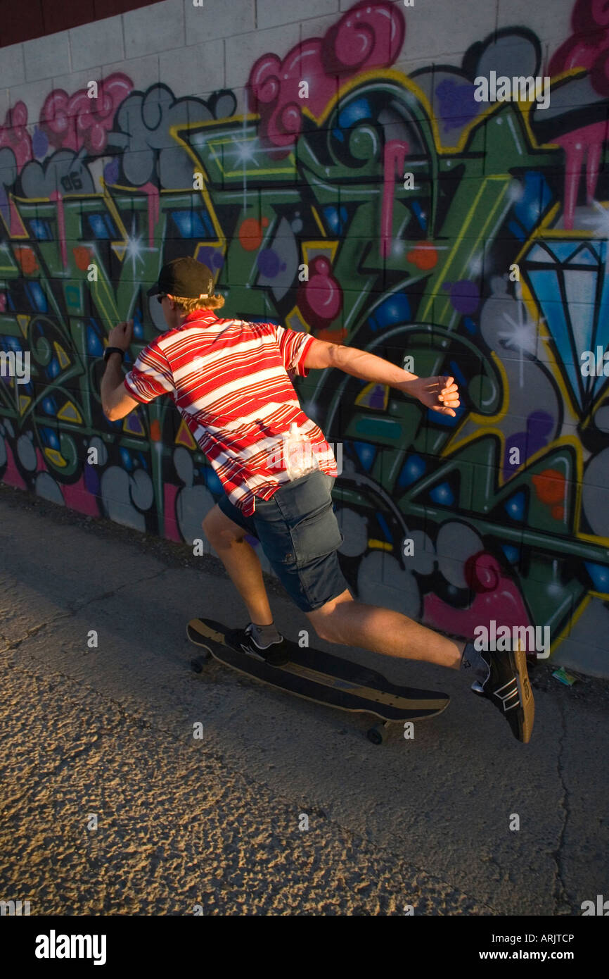 Vista trasera de un hombre skateboarding a lo largo de una pared cubierta de graffiti, Reno, Nevada, EE.UU. Foto de stock