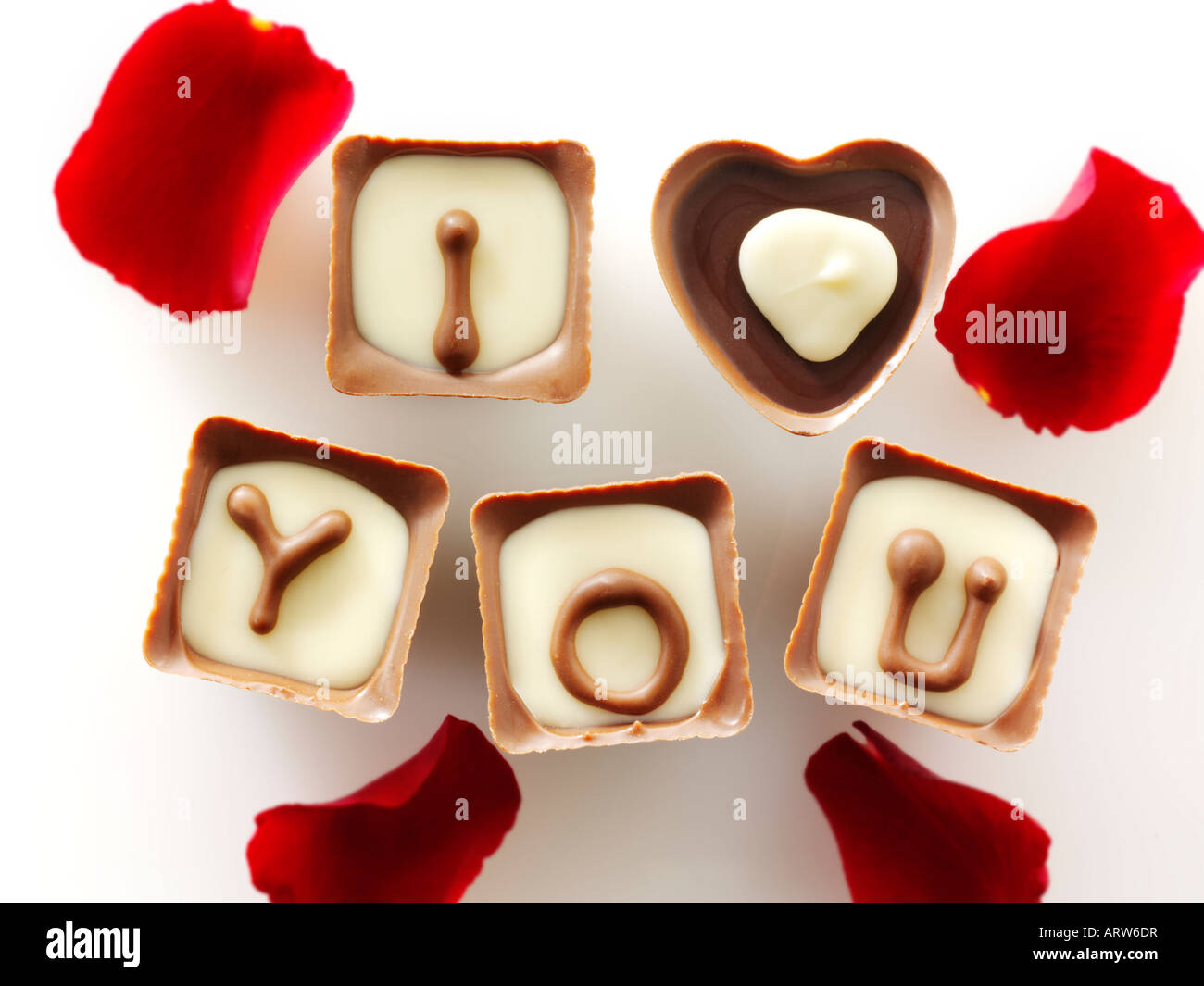 Te amo escrito en rojo en forma de corazón con pétalos de rosa - chocolates recortada contra blanco Foto de stock