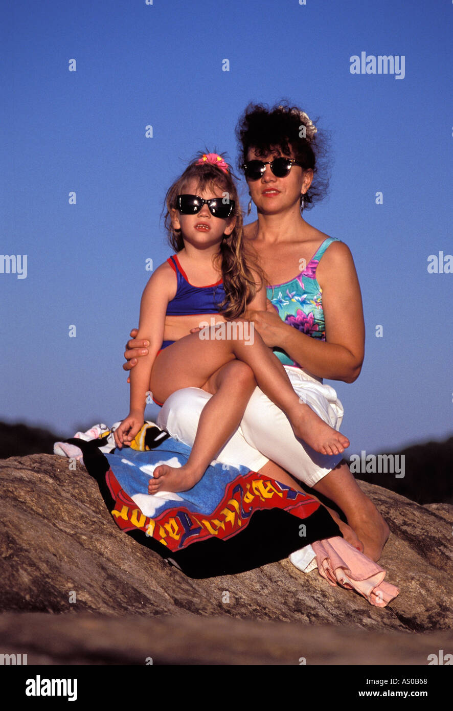Madre e hija con gafas de sol sentado sobre una roca, Connecticut, EE.UU. Foto de stock