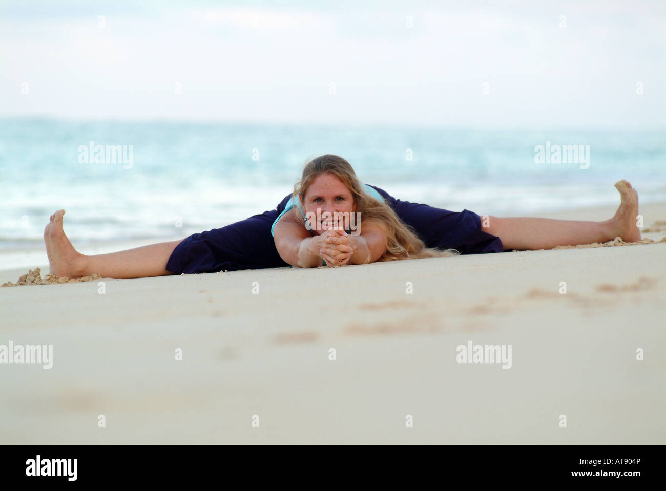 Mujer en el yoga se divide el estiramiento en la playa de arena blanca, Hawai Foto de stock