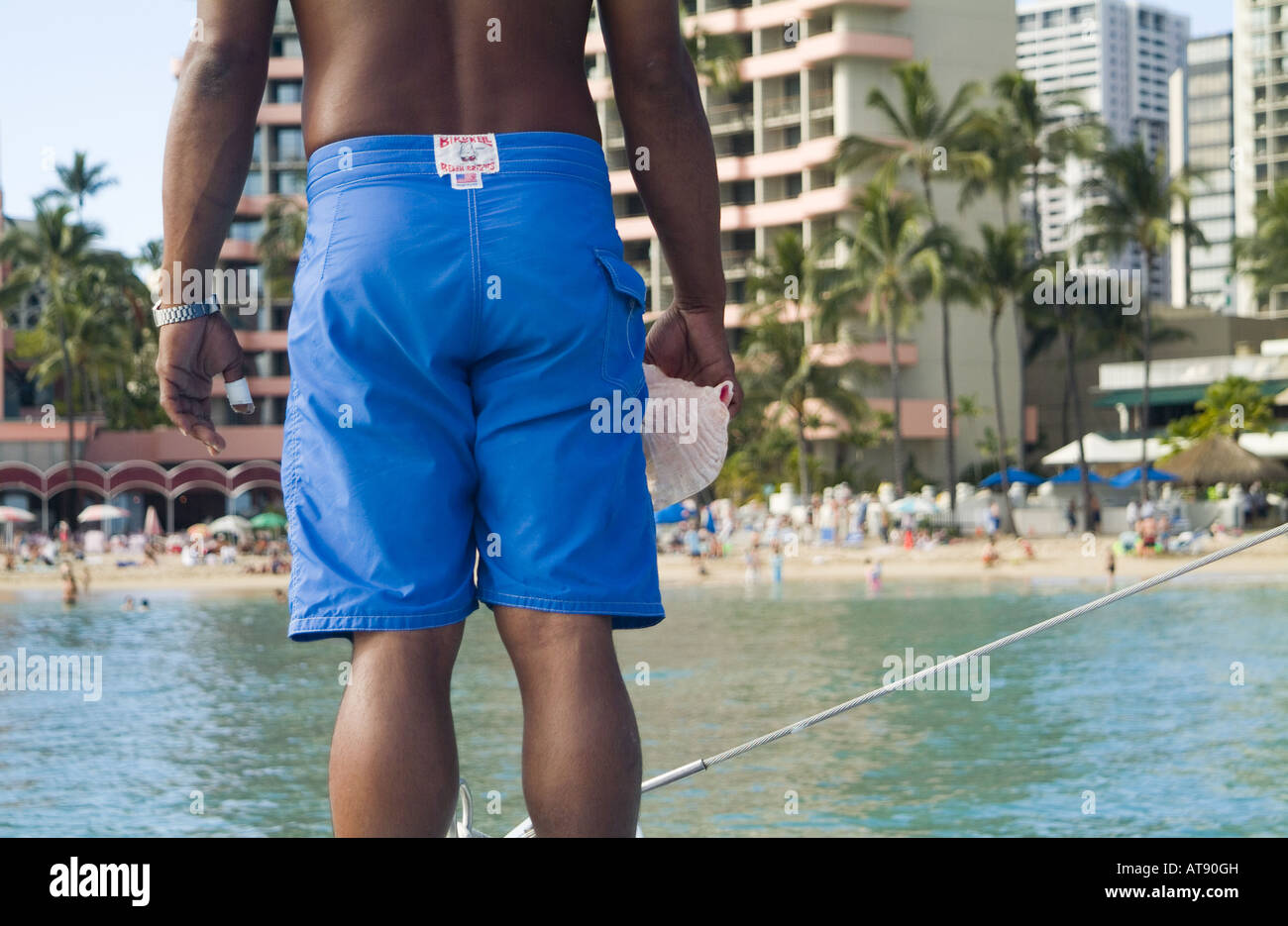 La vista posterior de un curtido hombre vestido con pantalones cortos de color azul brillante en la playa de Waikiki. Foto de stock