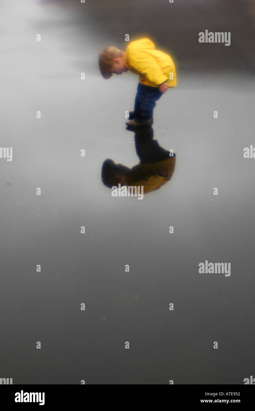 Niño pequeño jugando en el charco de agua lluvia slicker y reflexión Foto de stock