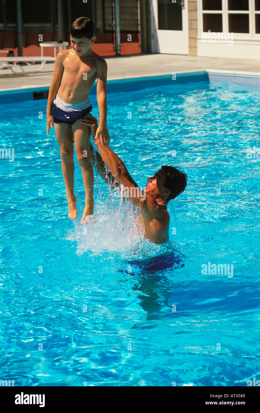Un padre alegremente lanza su hijo en el aire desde la piscina Foto de stock