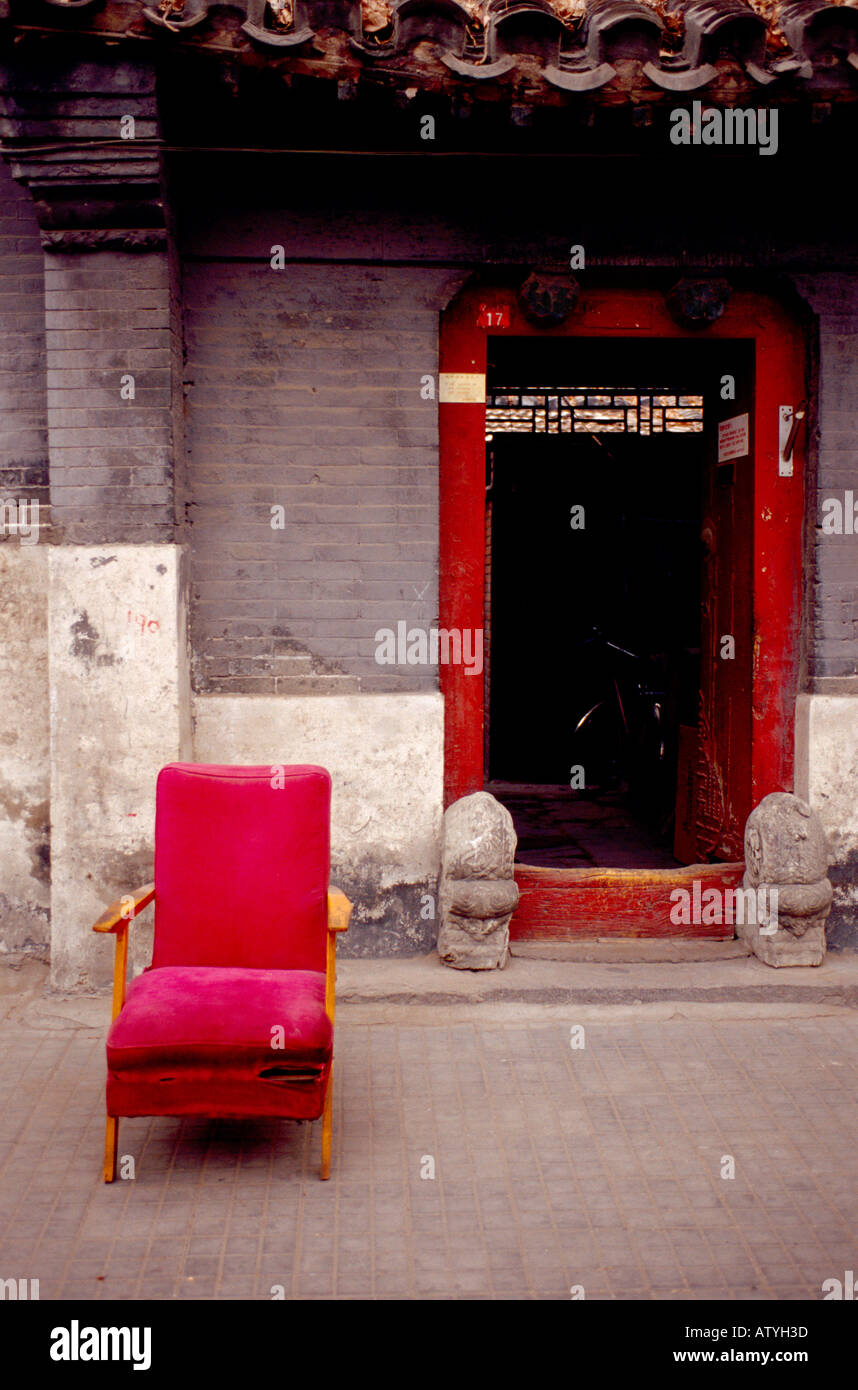 "Una vieja silla de terciopelo rojo fuera de la puerta de una casa típica de un hutong de Beijing China'. Foto de stock