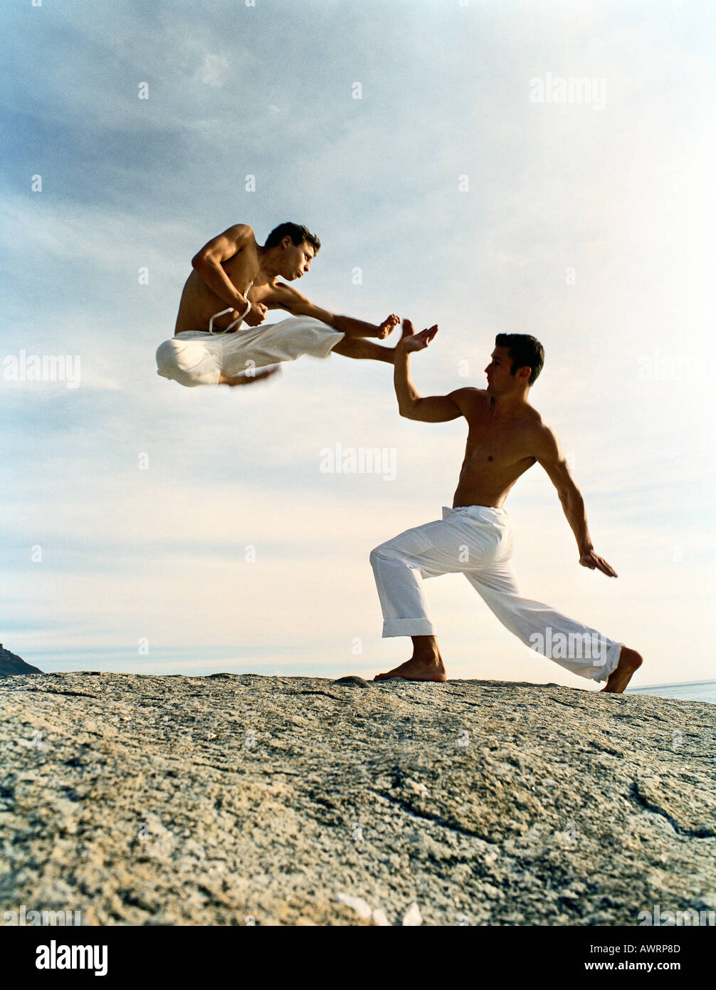 Dos hombres practicando las artes marciales en la tierra rocosa, uno en medio del aire, longitud completa Foto de stock