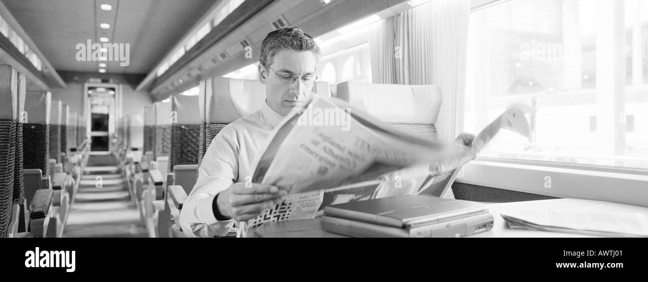 Empresario sentado en el tren la lectura de periódicos, b&W, vistas panorámicas Foto de stock