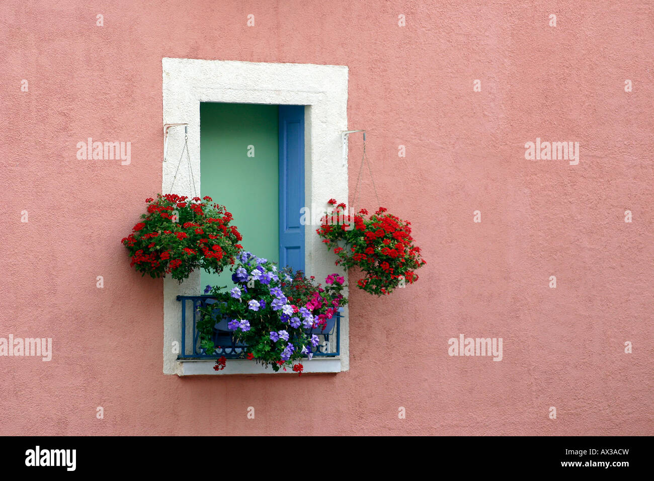 Ventana con coloridas flores en cestas colgantes y ventanales tomadas en Ortaffa en el sur de Francia. Foto de stock