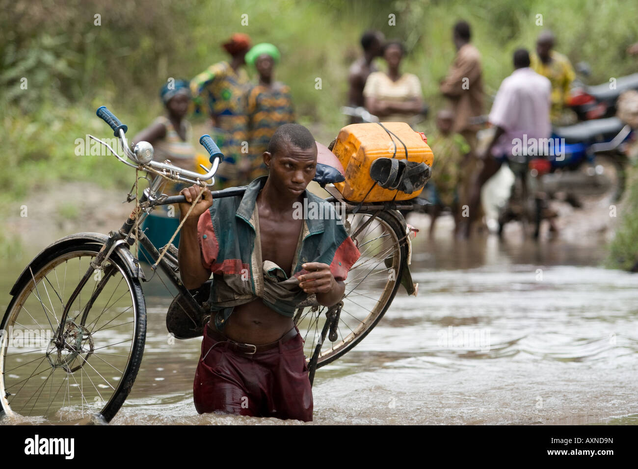 Un hombre lleva una bicicleta en su hombro cruzando un río desbordante Foto de stock