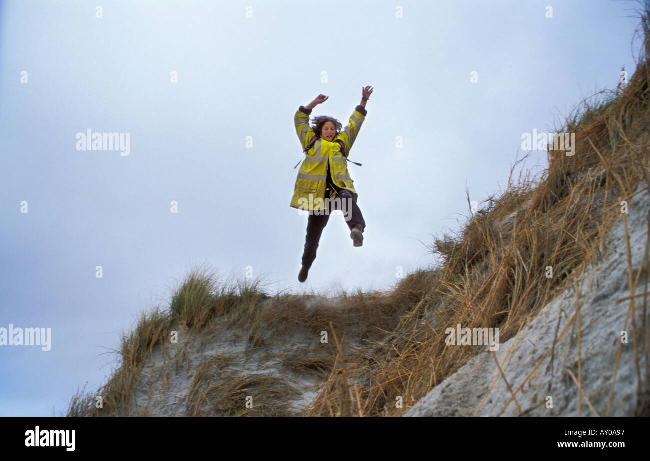 Salto de fe. Mujer de chaqueta de alta visibilidad saltando de una duna de arena. Foto de stock