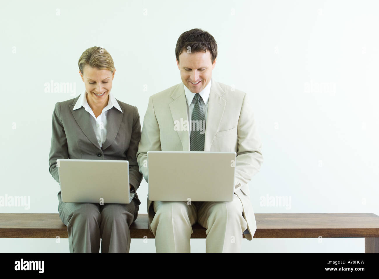 Asociados de negocios masculinos y femeninos sentados uno al lado del otro, ambos utilizando ordenadores portátiles Foto de stock