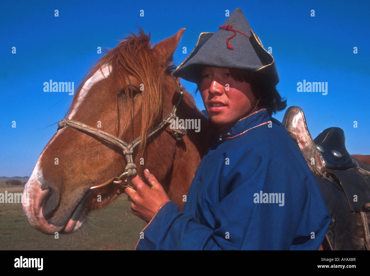 Granja de Mongolia boy en vestimentas tradicionales con su caballo en la granja en Hulun Buir pastizales del noreste de Mongolia Interior. Foto de stock