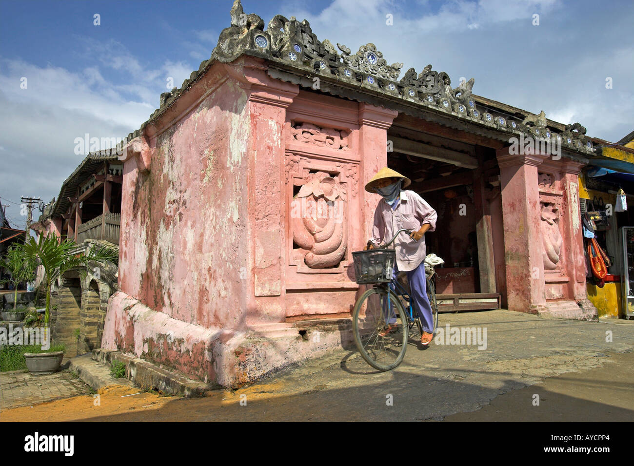 Mujer sombrero cónico en bicicleta sale del siglo XVII, el puente cubierto japonés de Hoi An ciudad histórica Vietnam Foto de stock