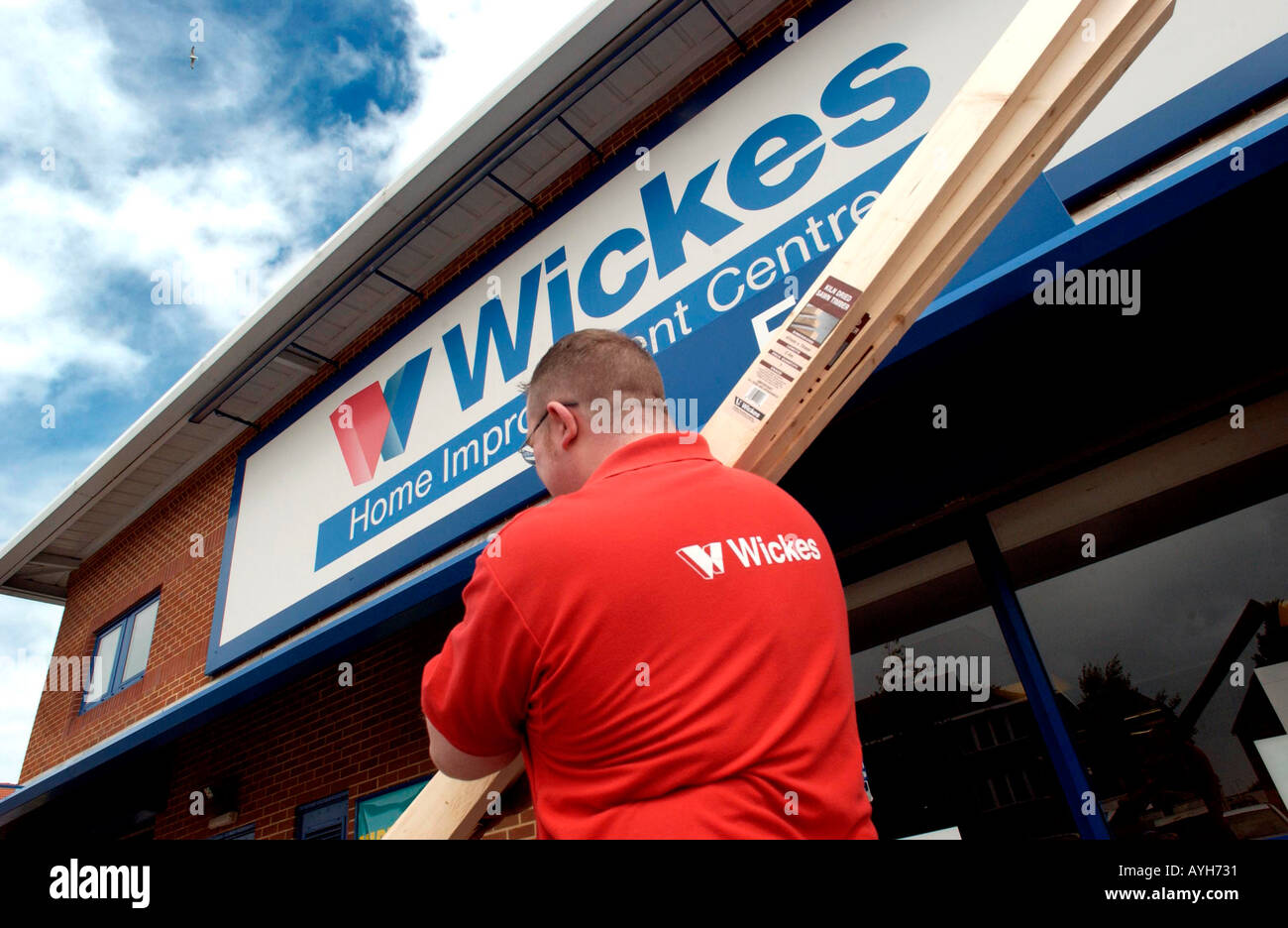 Un hombre en una tienda de bricolaje Wickes rojo tshirt lleva la madera. Foto de stock