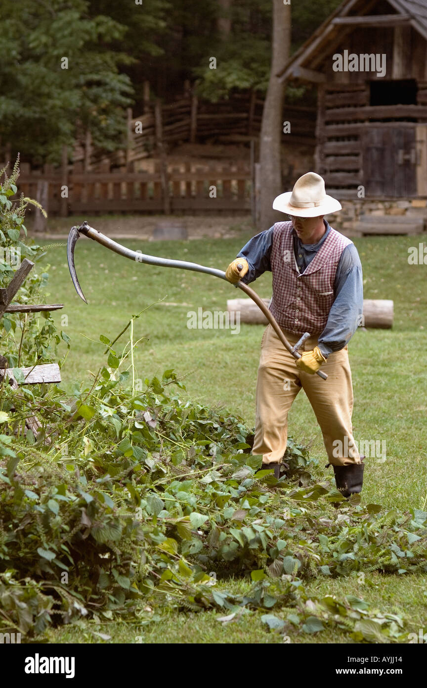 Hombre en trajes de época con guadaña para reducir las malas hierbas en la granja de la tierra entre los lagos Homeplace Tennessee Foto de stock