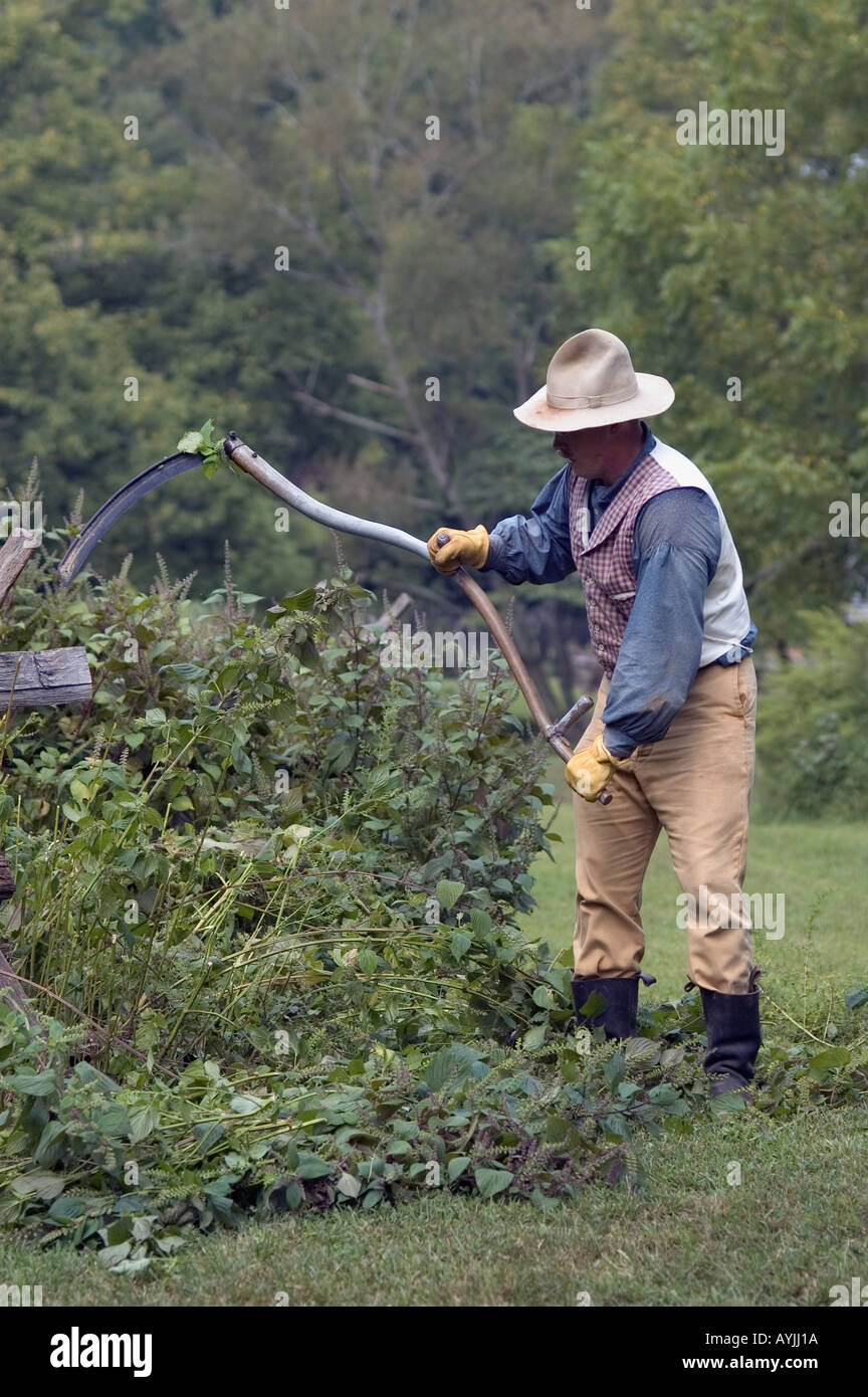 Hombre en trajes de época con guadaña para reducir las malas hierbas en la granja de la tierra entre los lagos Homeplace Tennessee Foto de stock
