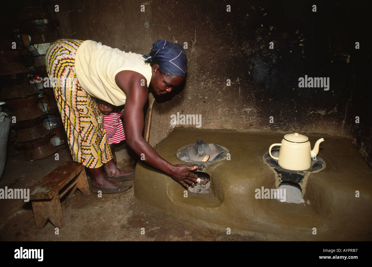 Mujer encendiendo su nueva estufa mejorada, de combustible eficiente, hecha de arcilla por la cooperativa de mujeres locales. Kisumu, Kenia Foto de stock