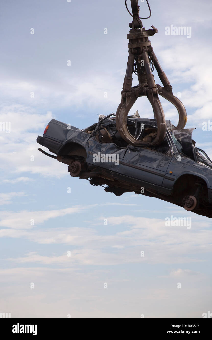 Agarre el gancho de una grúa levanta un coche destrozado por el cielo Foto de stock