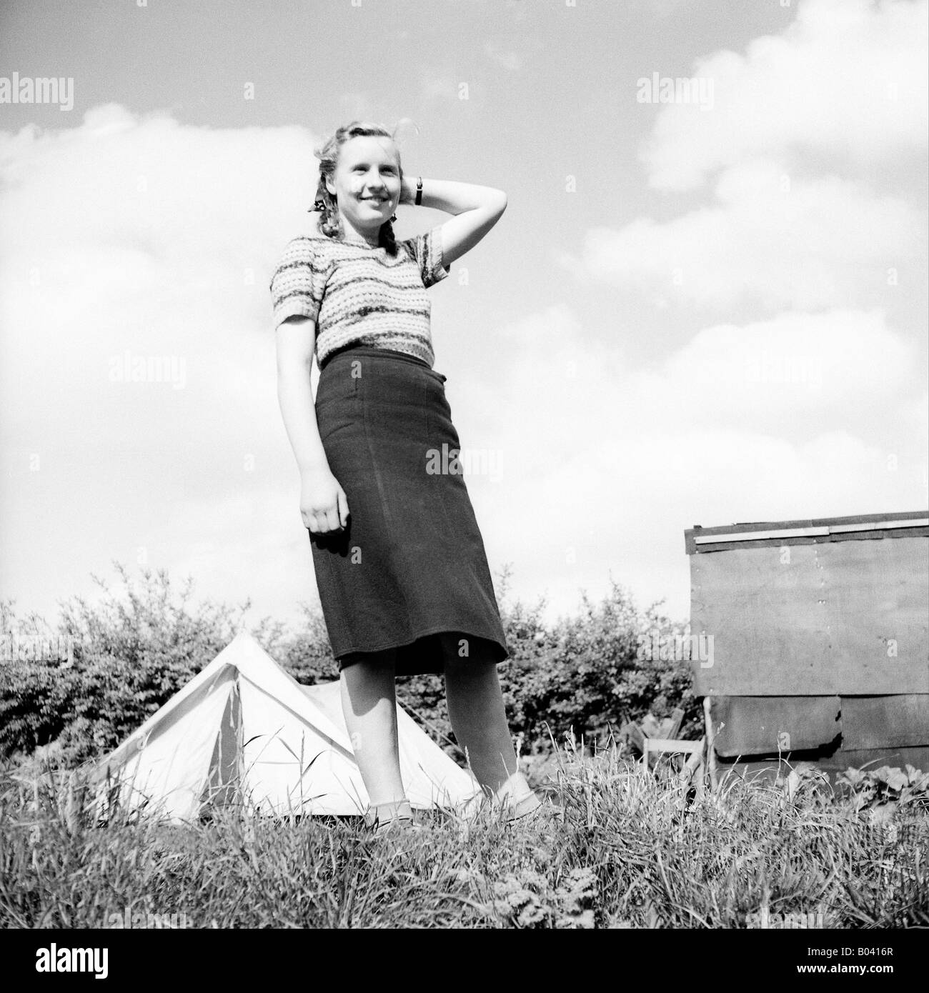 Antigua fotografía instantánea de la familia vintage de joven atractiva mujer rubia de pie delante de la tienda de campaña en el campamento de vacaciones Foto de stock