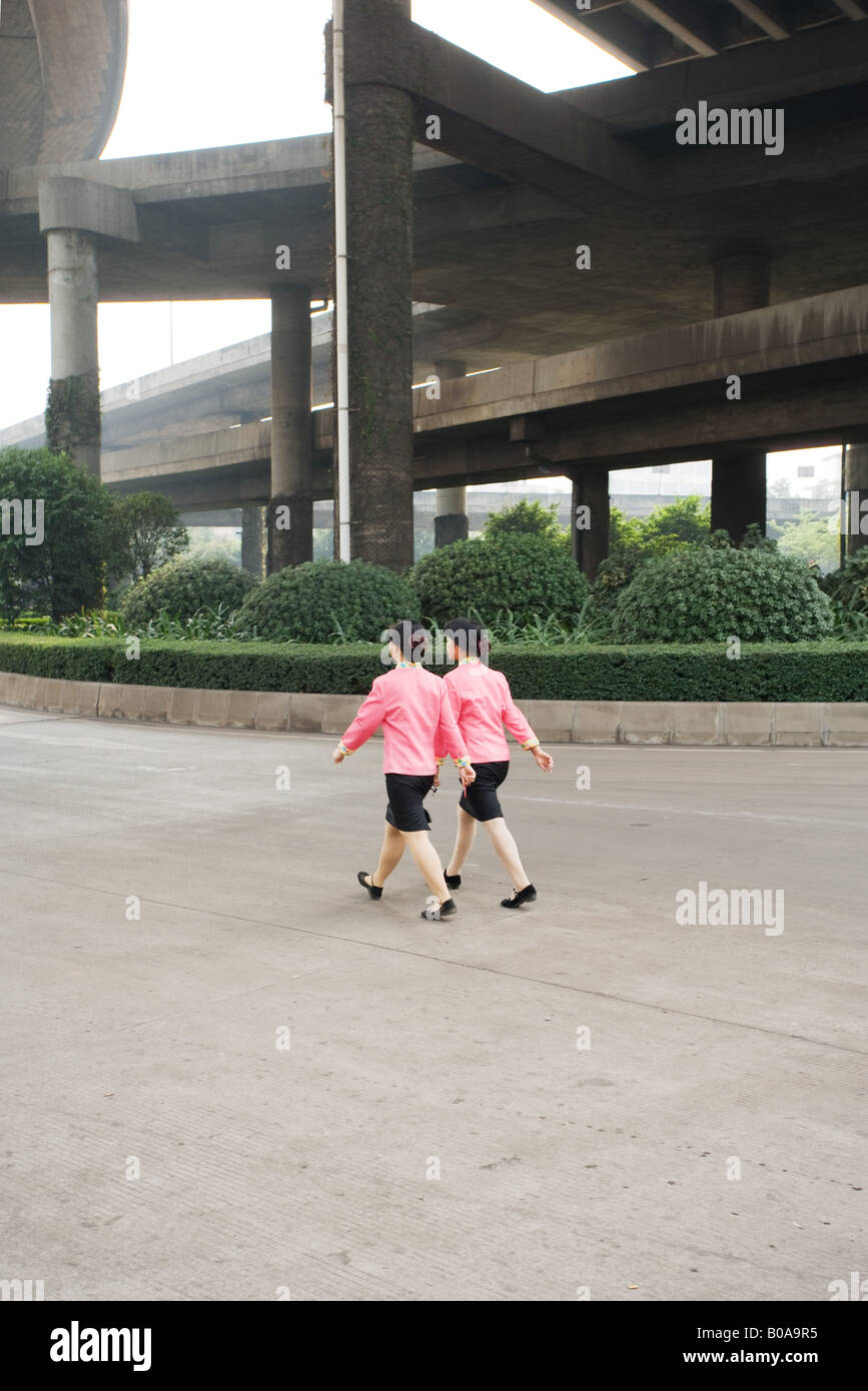 China, Guangzhou, dos mujer vistiendo uniformes coincidente caminando debajo del puente, vista trasera Foto de stock