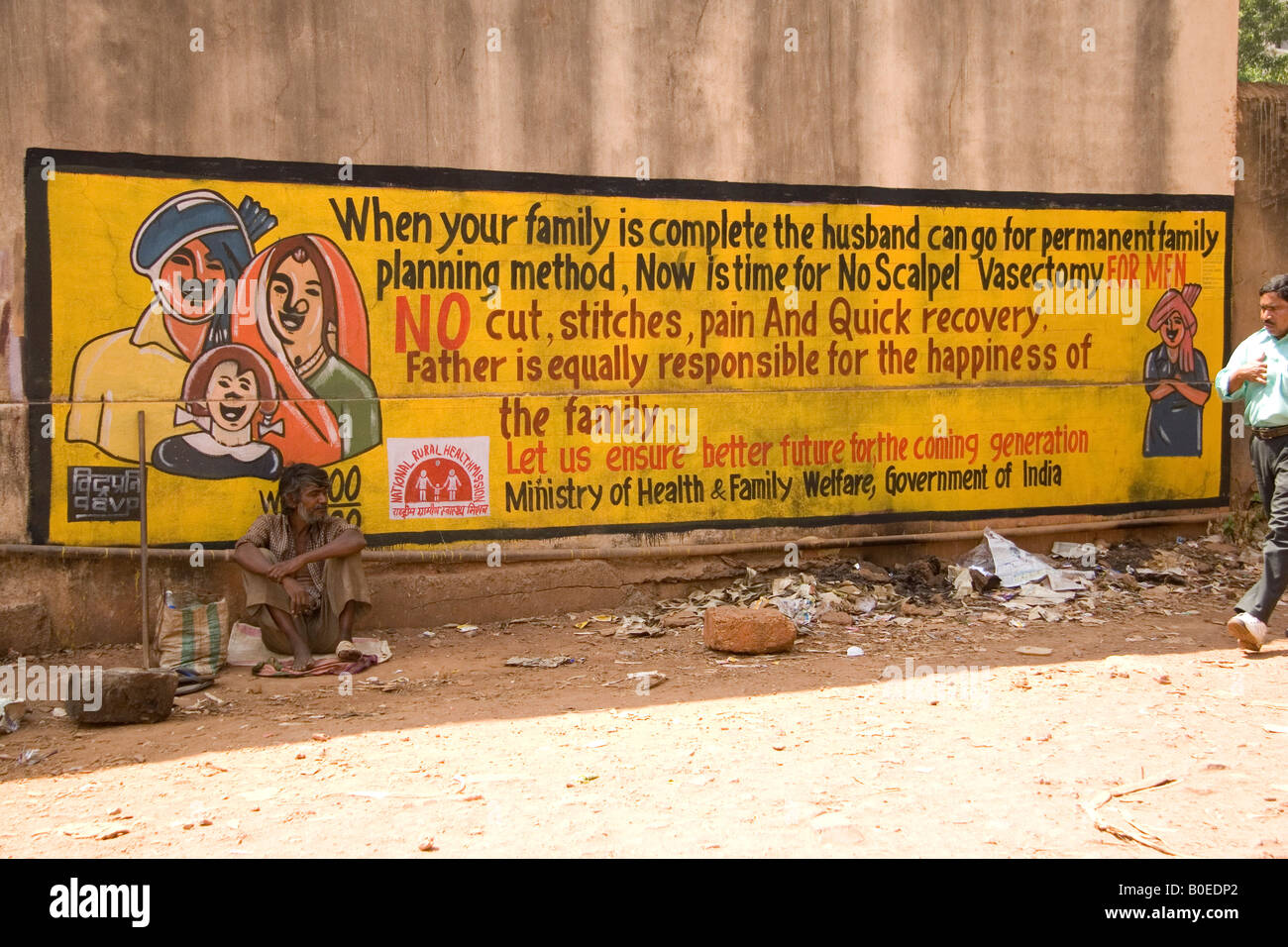 Un hombre se sienta junto a un anuncio que ensalza el valor de la planificación familiar en la ciudad de Panaji, Goa, India. Foto de stock