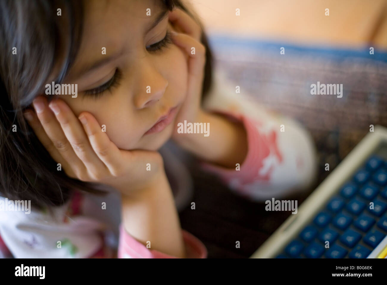 Cuatro años de edad, niña juega con su ordenador portátil de juguete tumbado en el suelo, la cabeza entre las manos Foto de stock
