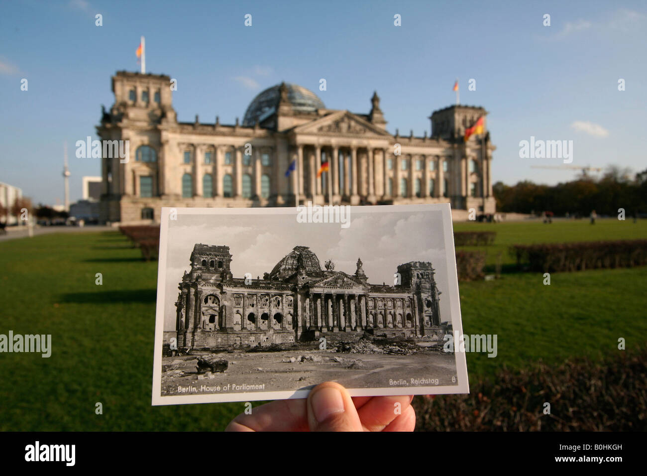Entonces, como ahora, la mano sosteniendo una vieja foto en blanco y negro del Reichstag alemán o Casas del Parlamento mostrando la WWII bomb d Foto de stock