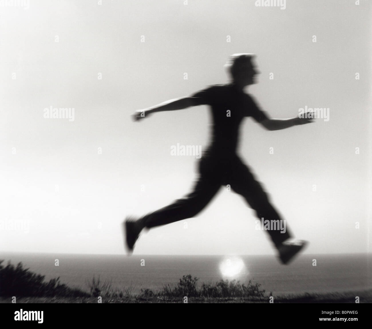 Silueta de hombre saltando en el aire con las piernas por Sun bajo el océano en blanco y negro Foto de stock