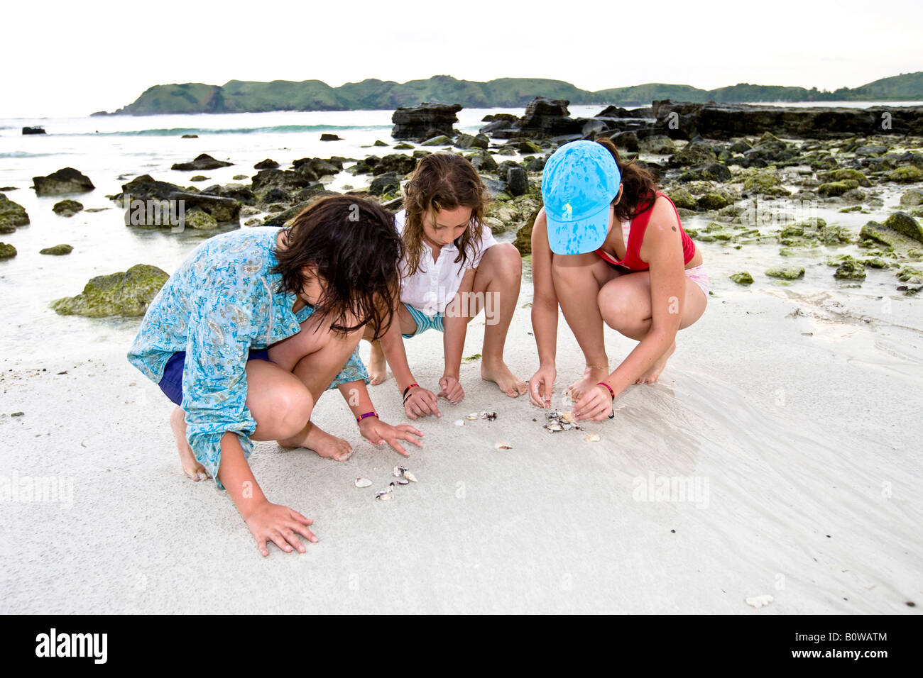 Los niños buscando conchas y arrecifes a lo largo de una playa desierta, la isla de Lombok, Lesser Sunda Islands, Indonesia Foto de stock
