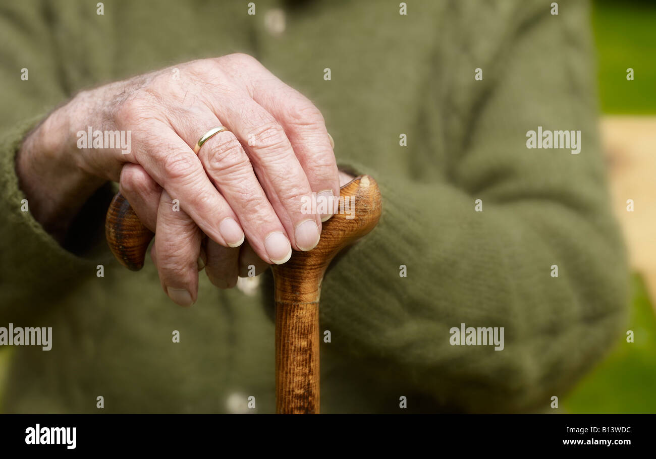 Anciano sentado con sus manos en un bastón Foto de stock