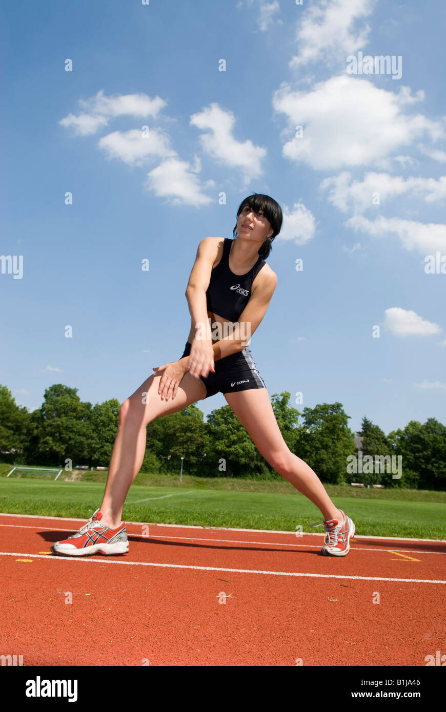 Mujer joven con vestimenta deportiva estiramientos en una pista de