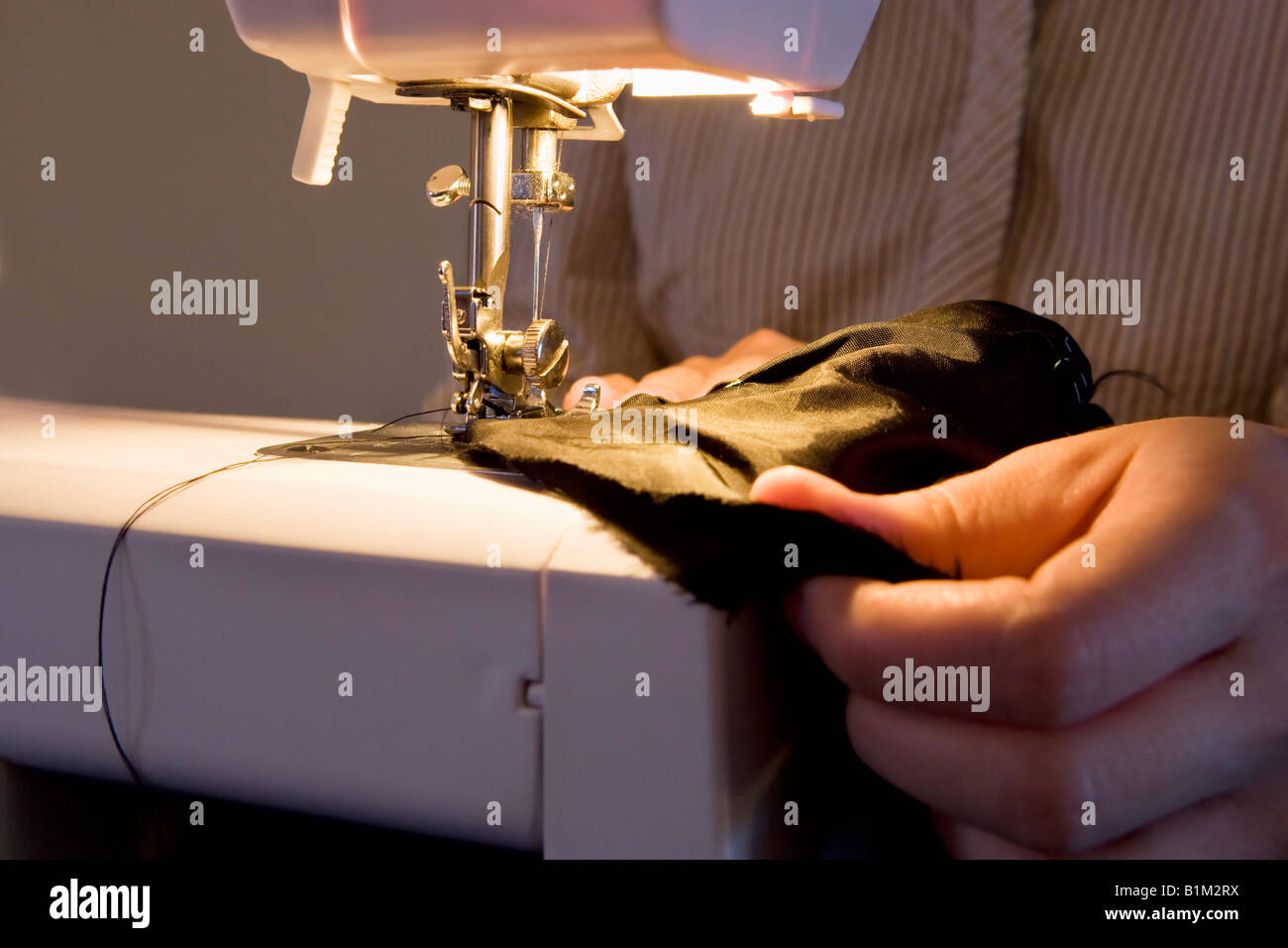 Cerca de una mujer que utiliza una máquina de coser en puntada tela negra. Foto de stock