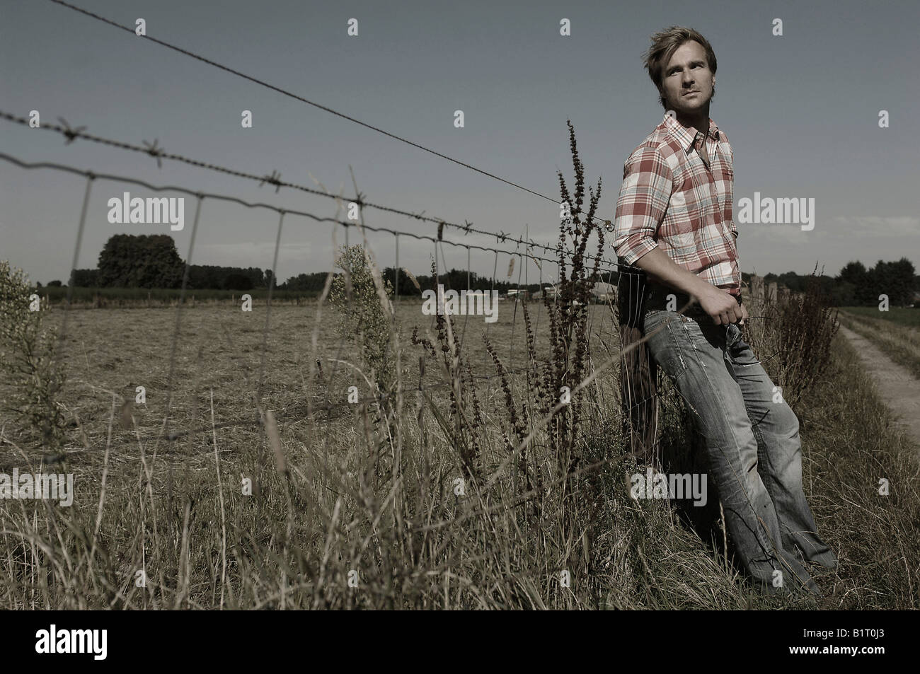 33-año-viejo hombre vestido como un vaquero, apoyado contra una valla de  alambre de púa Fotografía de stock - Alamy