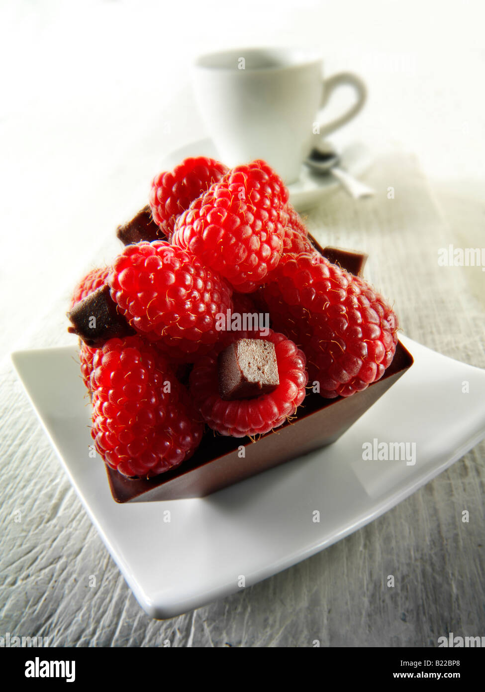 Una pastelería hecha a mano especialidad rica en deliciosas tortas de chocolate relleno de frambuesas frescas con café en un ambiente blanco Foto de stock