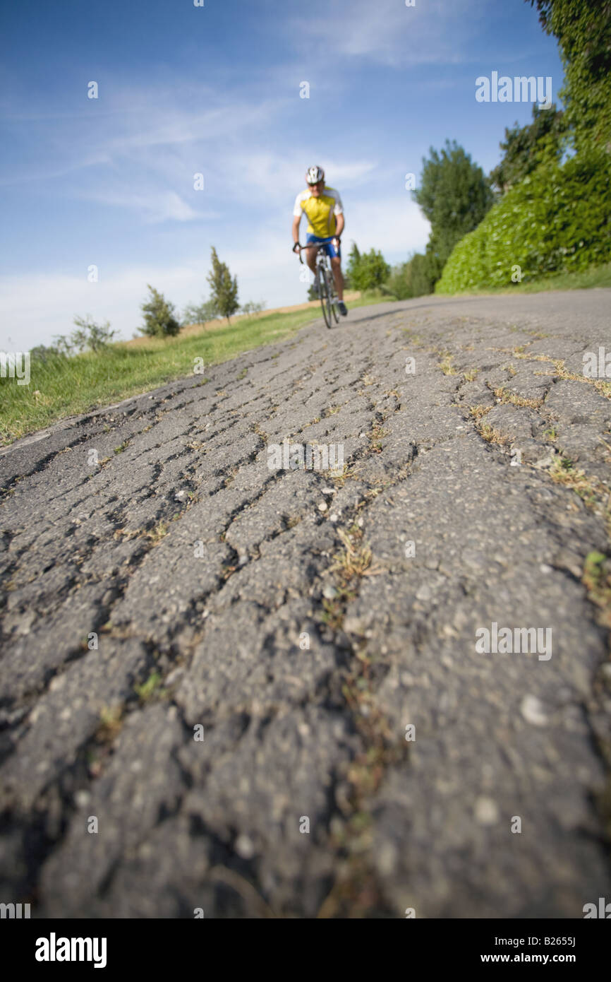 Bicicleta equitación ciclista en una carretera agrietada, vista frontal Foto de stock