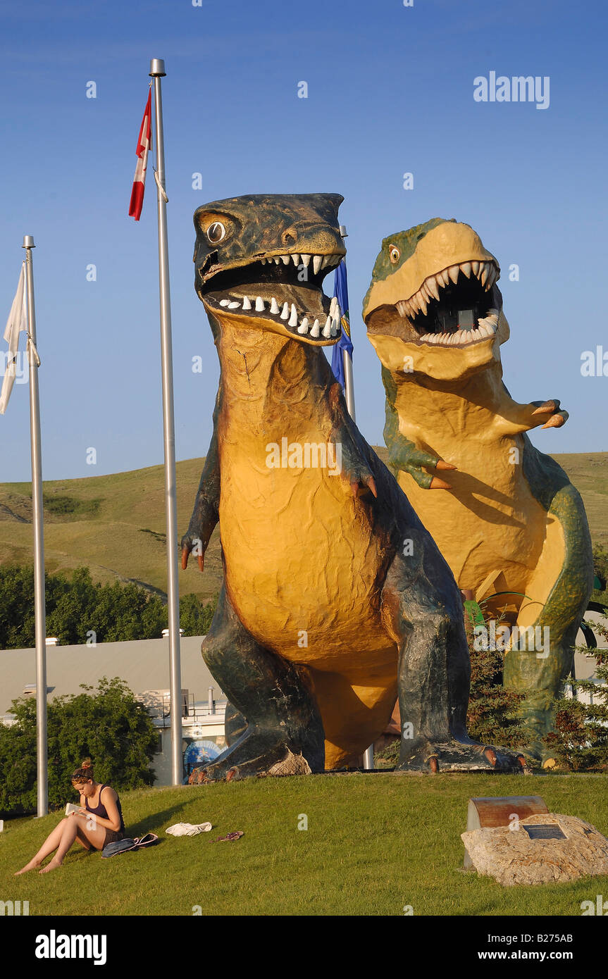 Mire detrás de usted! Par de modelos gigantes de Tyrannosaurus Rex Dinosaurios en Drumheller y una niña leyendo, Alberta, Canadá Foto de stock