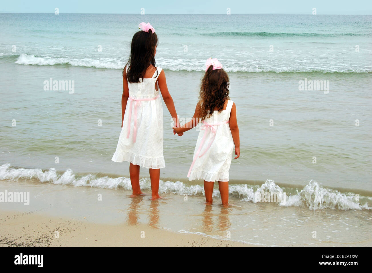 Las niñas en vestidos blancos tomados de la mano por la playa Fotografía de  stock - Alamy