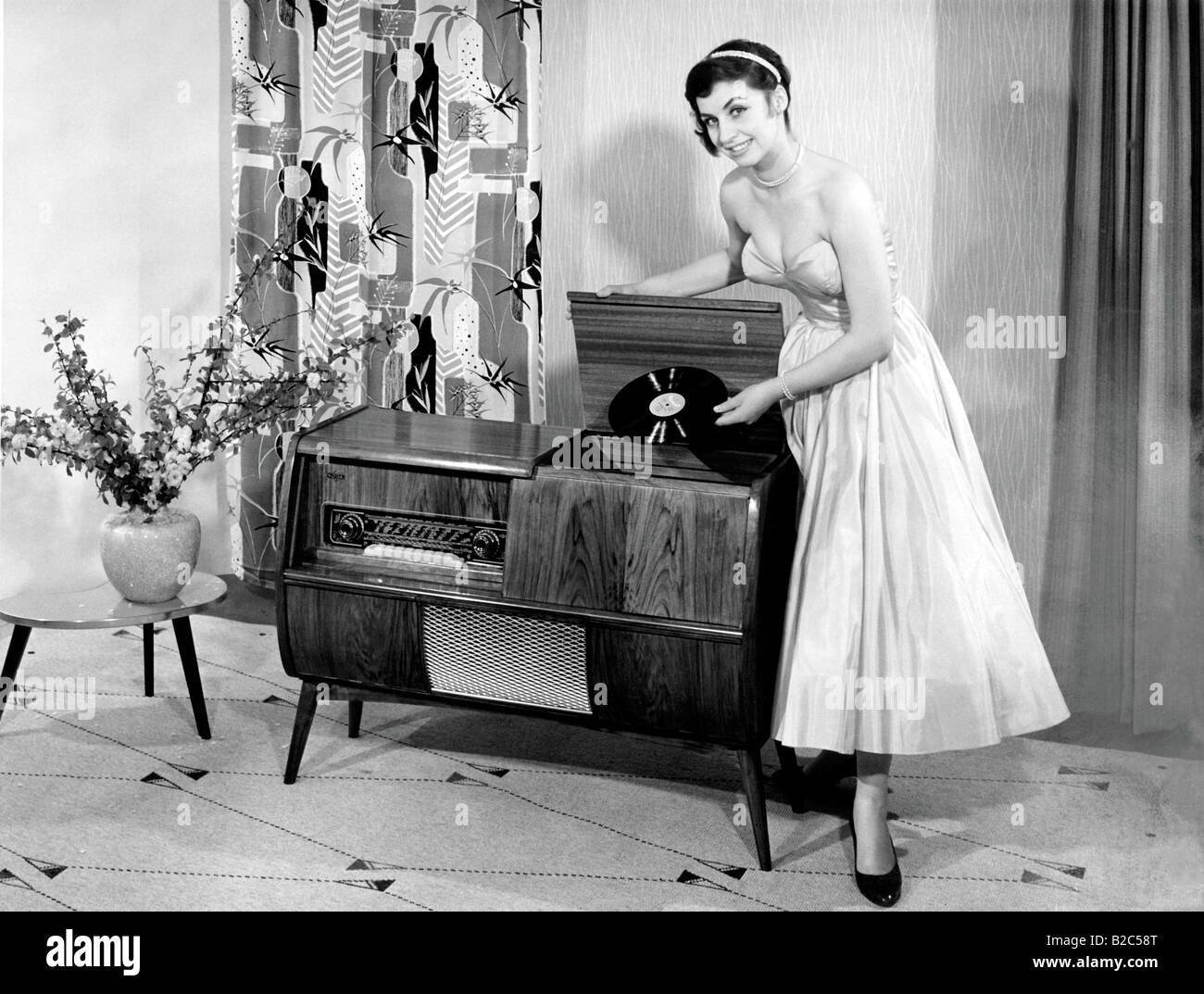 Mujer posando junto a un tocadiscos, mantiene un registro histórico de la imagen alrededor de 1955 Foto de stock