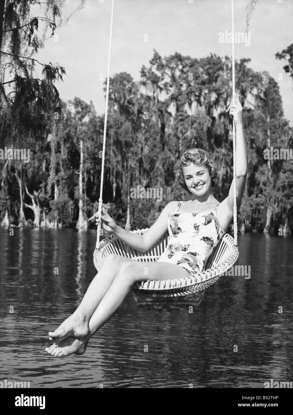 Retrato de una joven mujer sentada en un columpio en el lakeside y sonriente Foto de stock