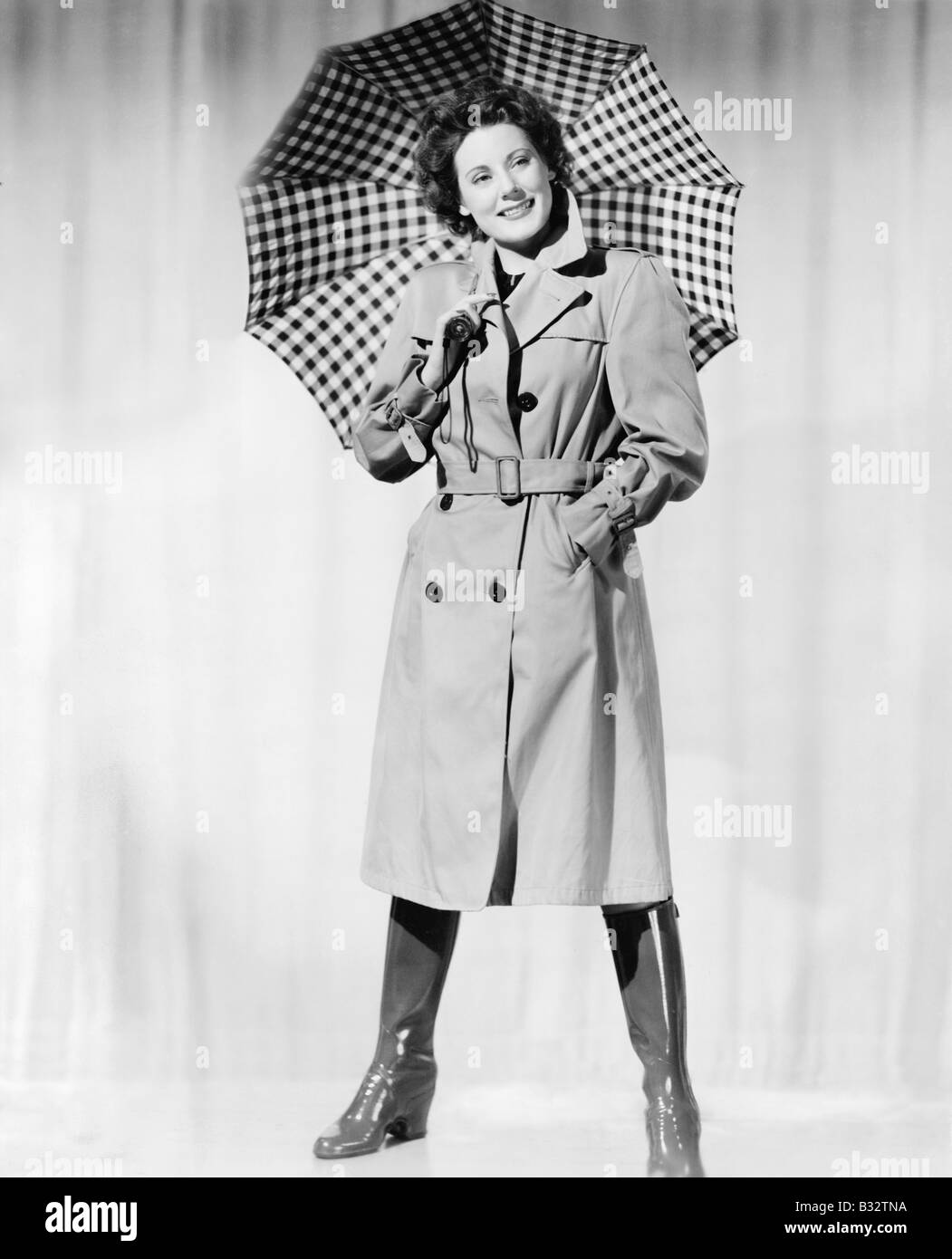 Mujer en ropa de lluvia y sonriente sosteniendo un paraguas Foto de stock