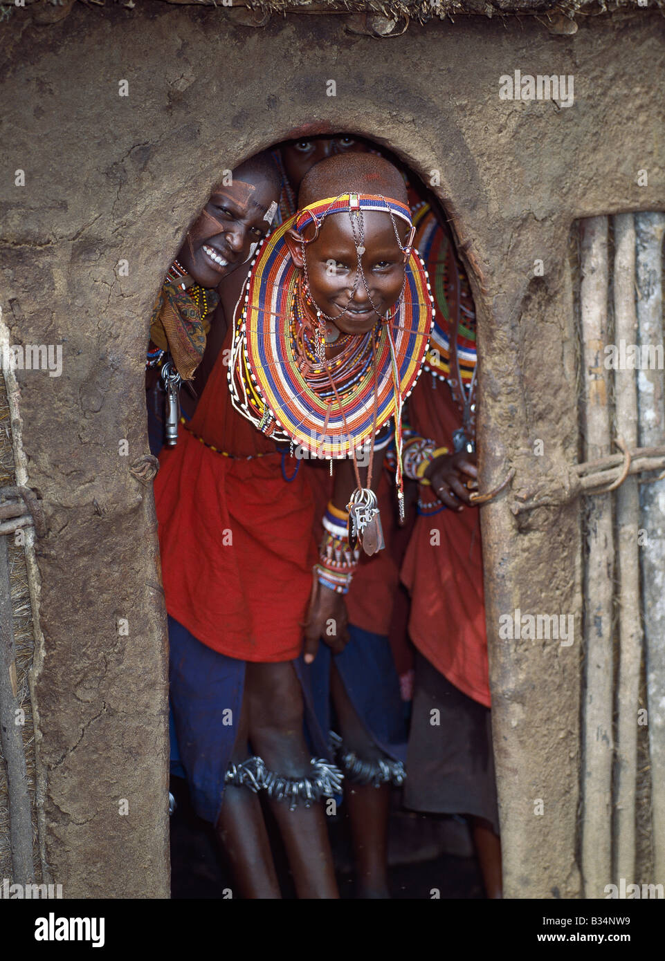 Kenya, Trans-Mara, Lolgorien. Las niñas masai en todos sus atavíos y con cascabeles atados redondear sus piernas espere en la entrada Foto de stock