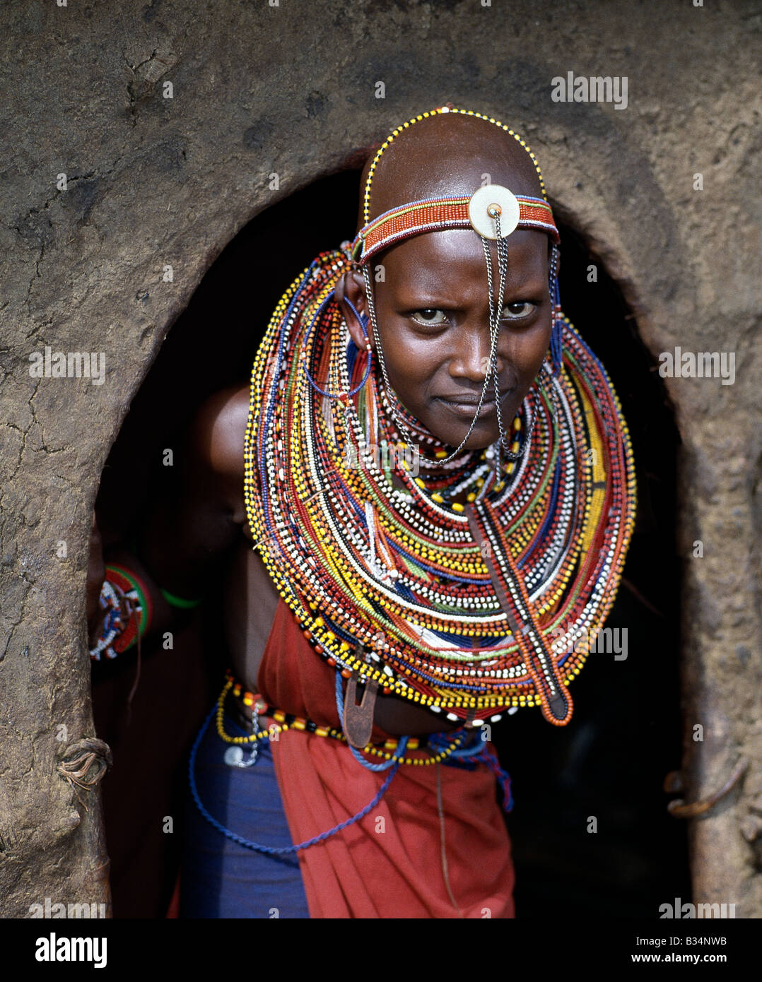 Kenya, Trans-Mara, Lolgorien. Una joven chica Maasai en todas sus galas se detiene en la entrada a la casa de su madre. Foto de stock