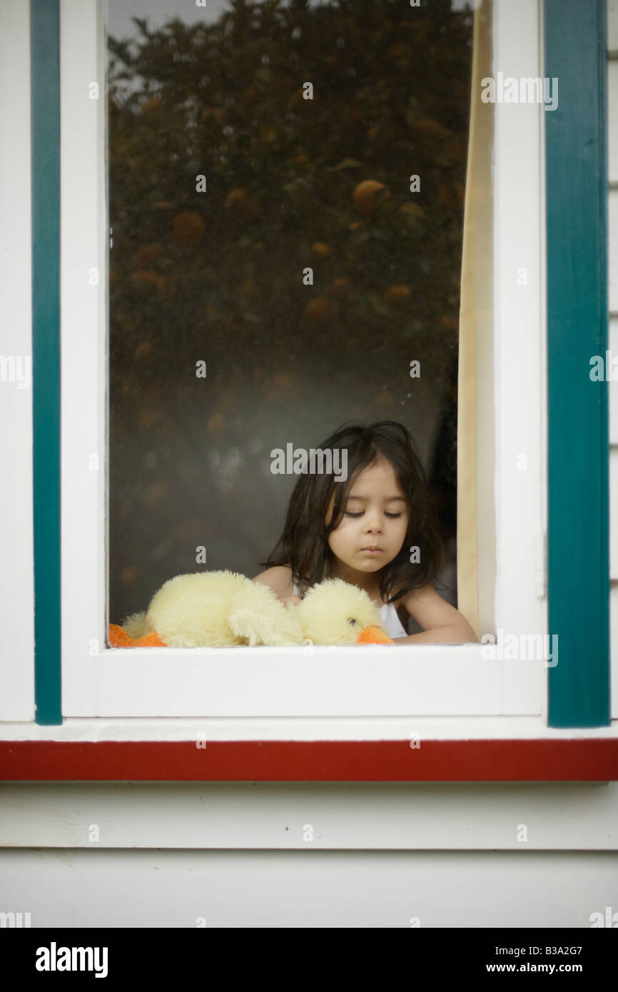 Muchacha envejecida 5 mira por la ventana sosteniendo un peluche pato Foto de stock